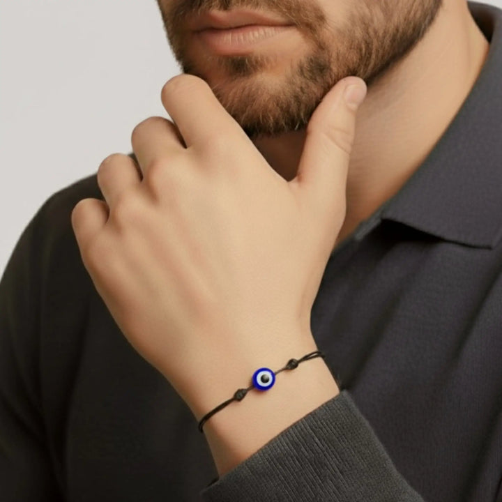 Person wearing a bracelet with an eye charm on a plain background