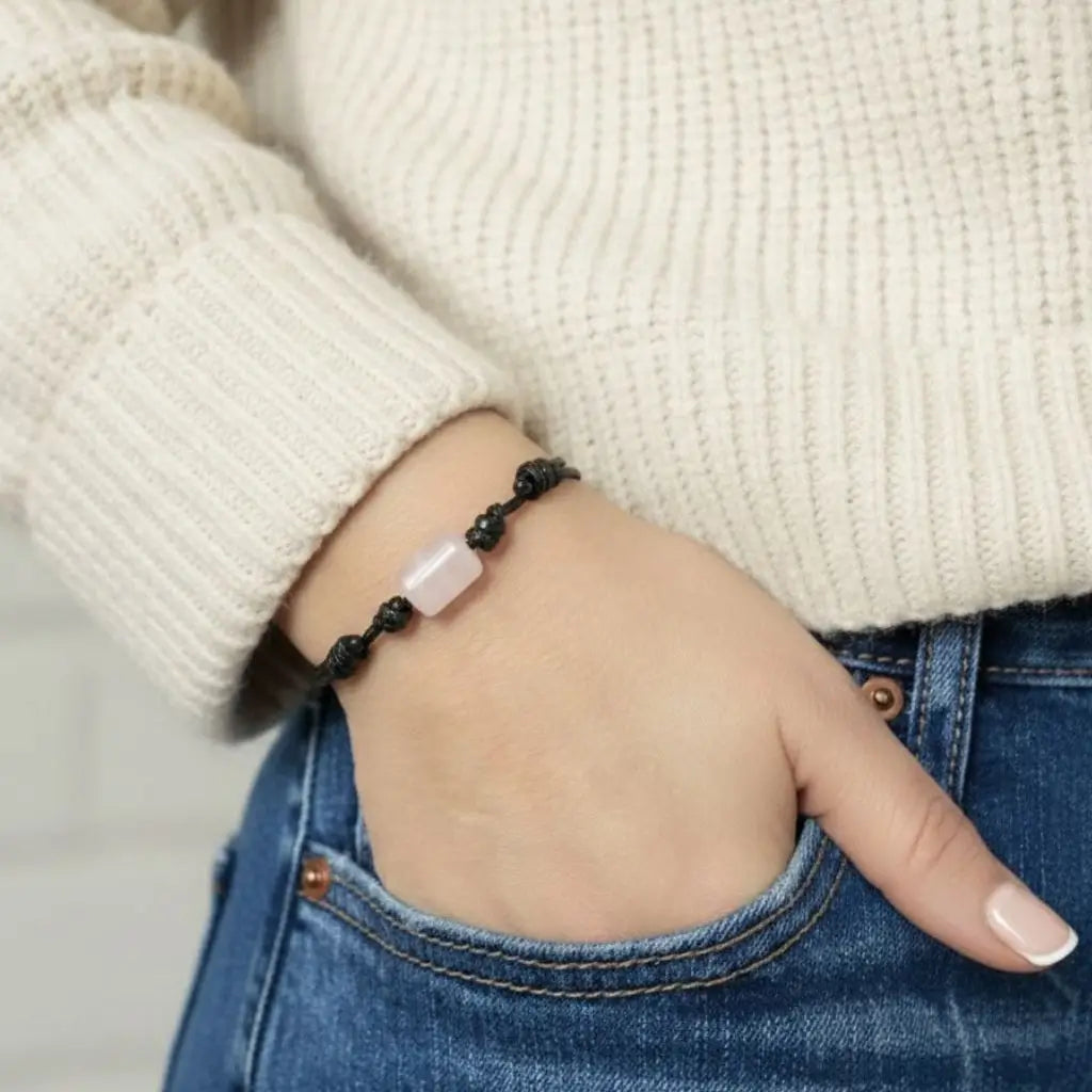 Hand wearing a black beaded bracelet with a rose quartz stone, against a neutral background.