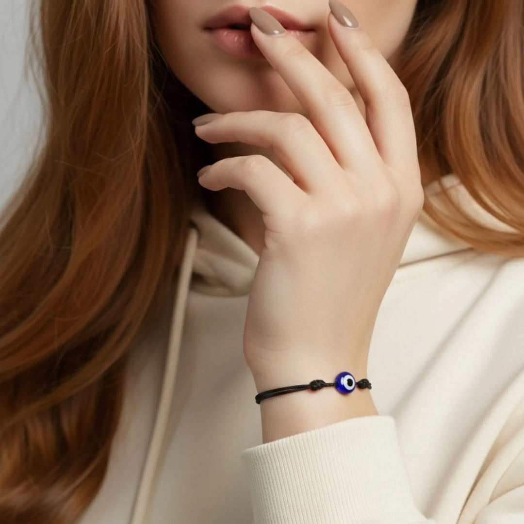 Close-up of a person wearing a bracelet with an eye charm, against a neutral background.