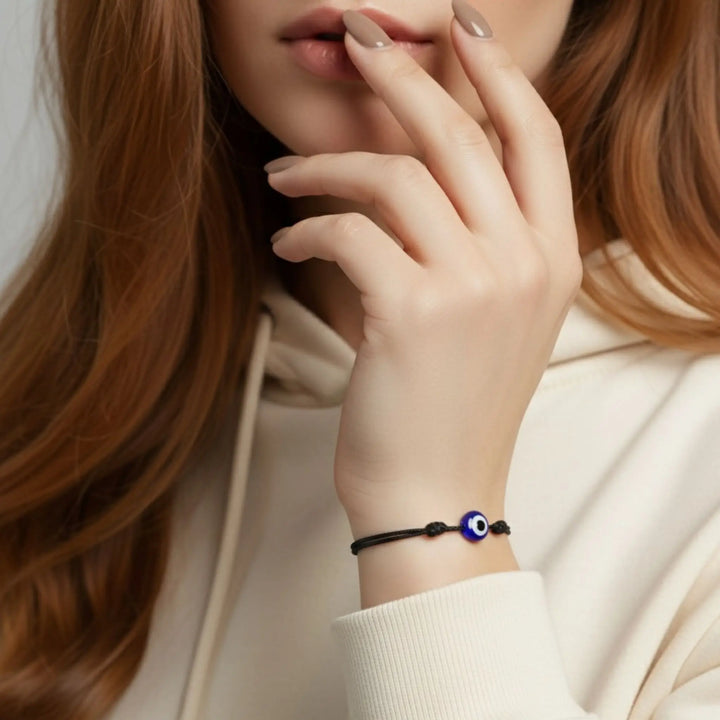 Close-up of a person wearing a bracelet with an eye charm, against a neutral background.