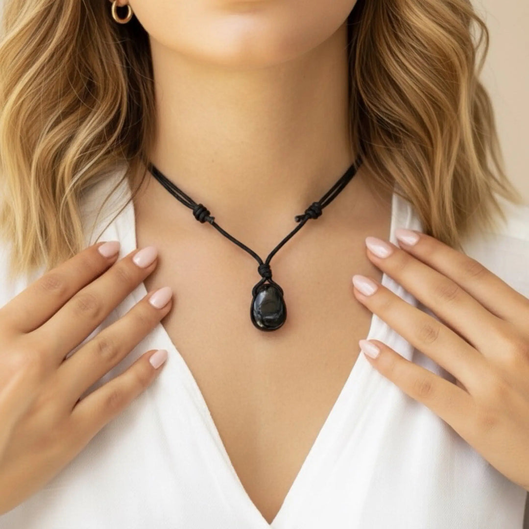 Woman wearing a black tourmaline  necklace with a pendant, hands gently touching her shoulders.