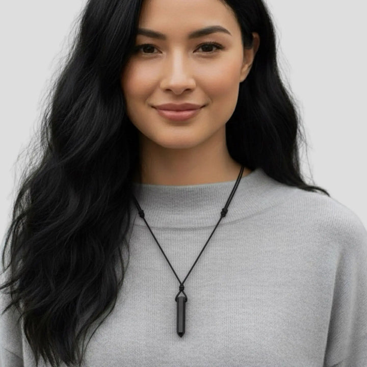 Woman wearing a black tourmaline pendant necklace against a plain background
