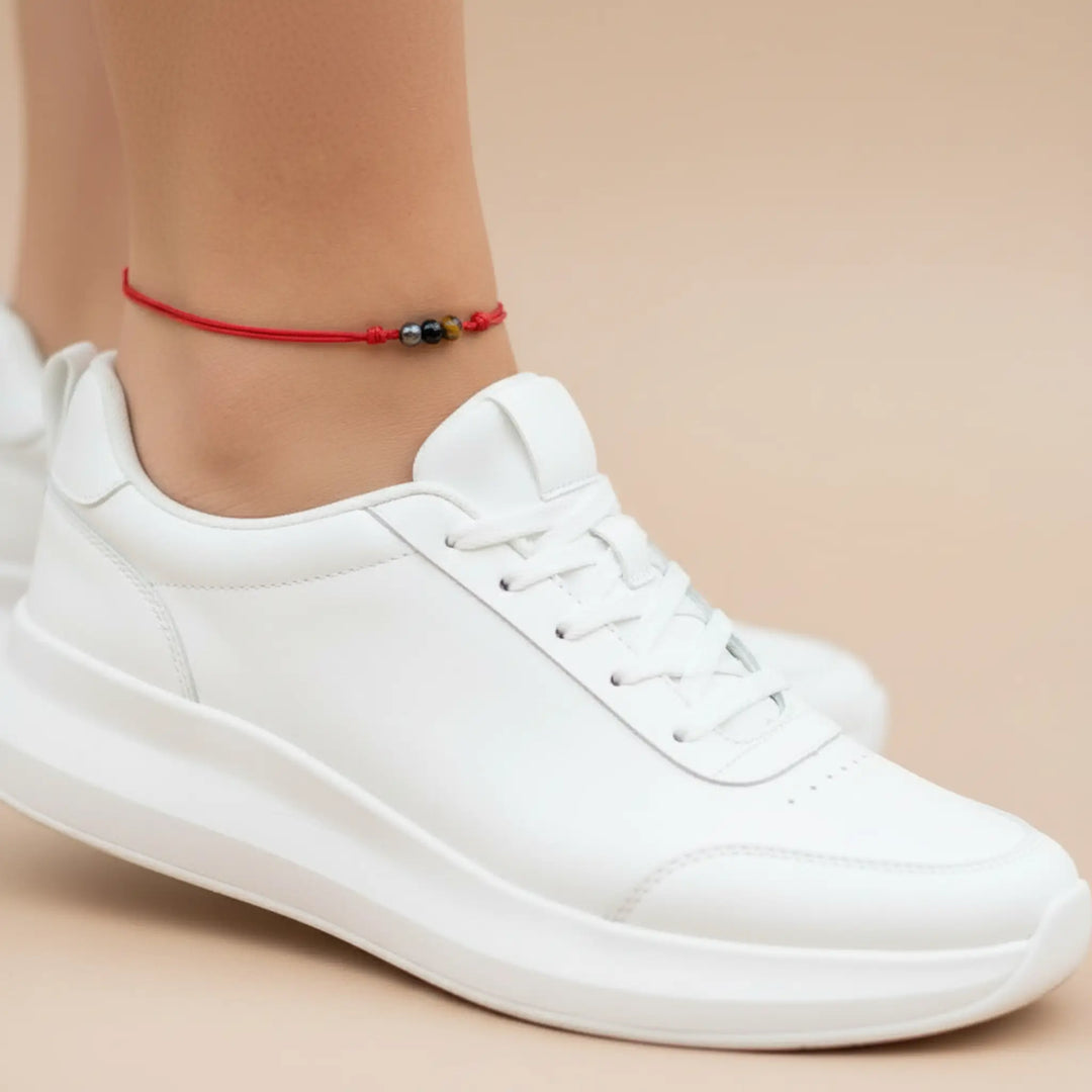 White sneakers worn with a red anklet on a beige background