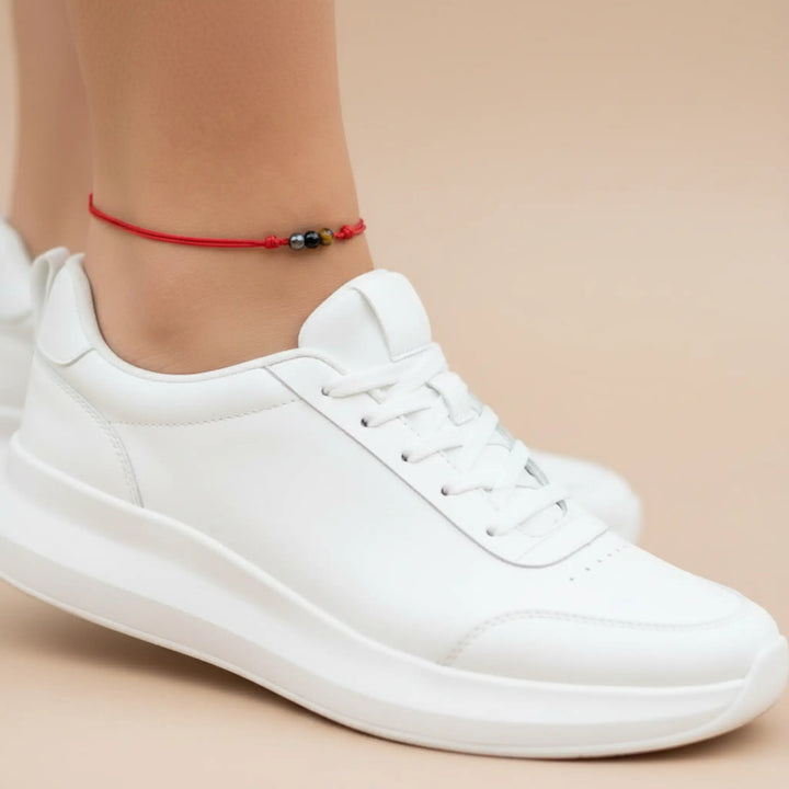 White sneakers worn with a red anklet on a beige background