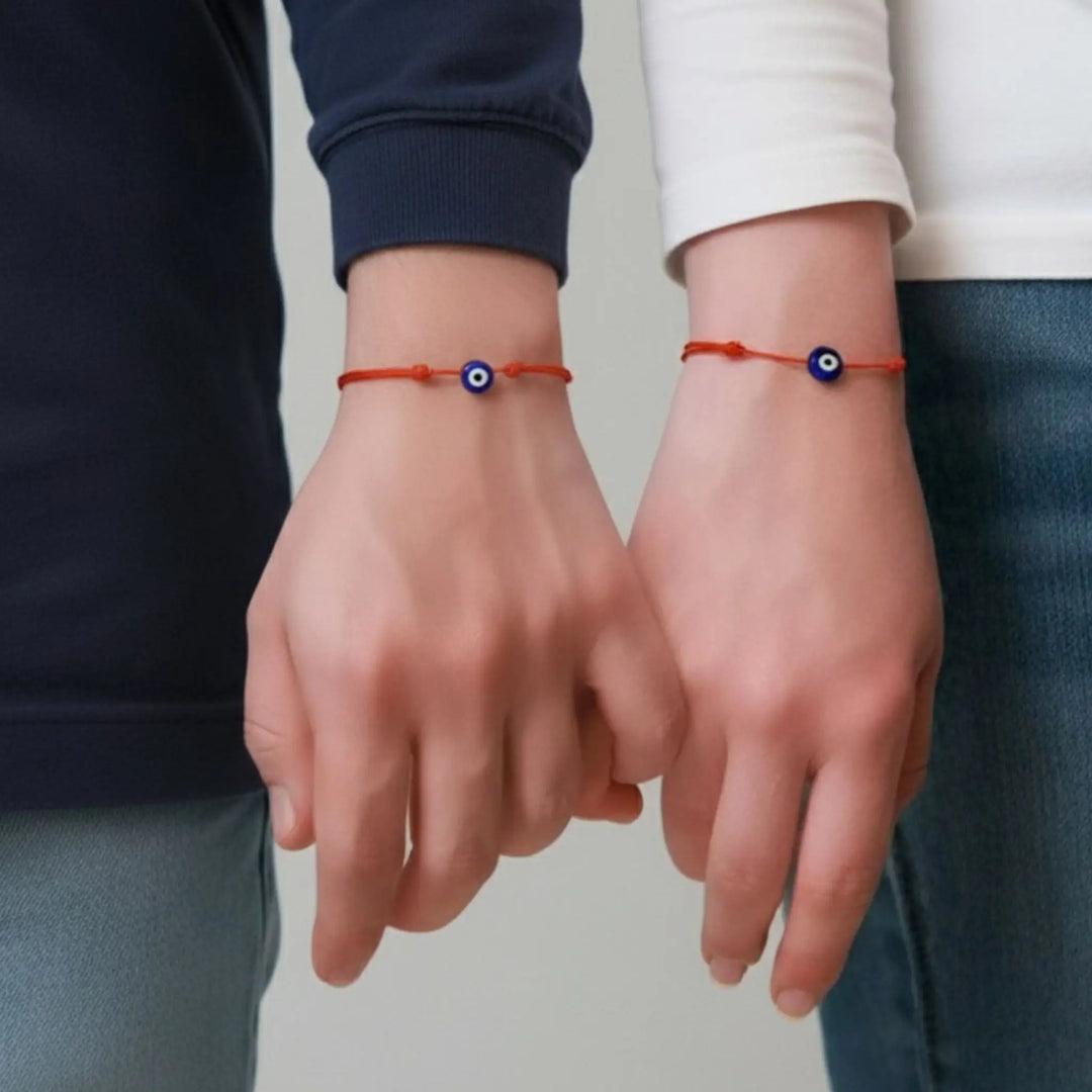 Two hands wearing red bracelets with blue evil eye symbols against a neutral background