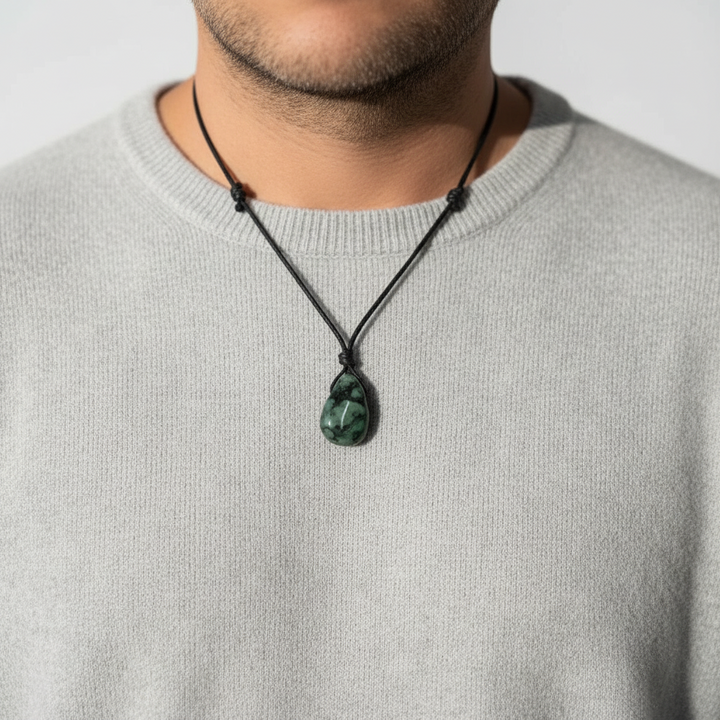 Person wearing a necklace with a green emeral pendant against a neutral background 