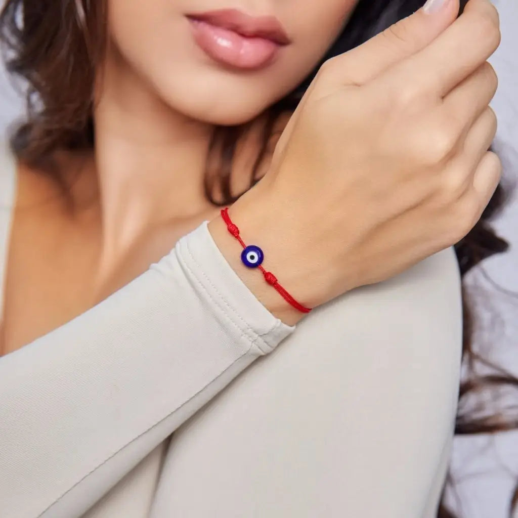 Red string bracelet with an evil eye charm on a woman's wrist, minimalist style.