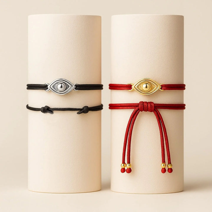 Two bracelets on cylindrical containers, one black with silver eye charm and one red with gold eye charm.