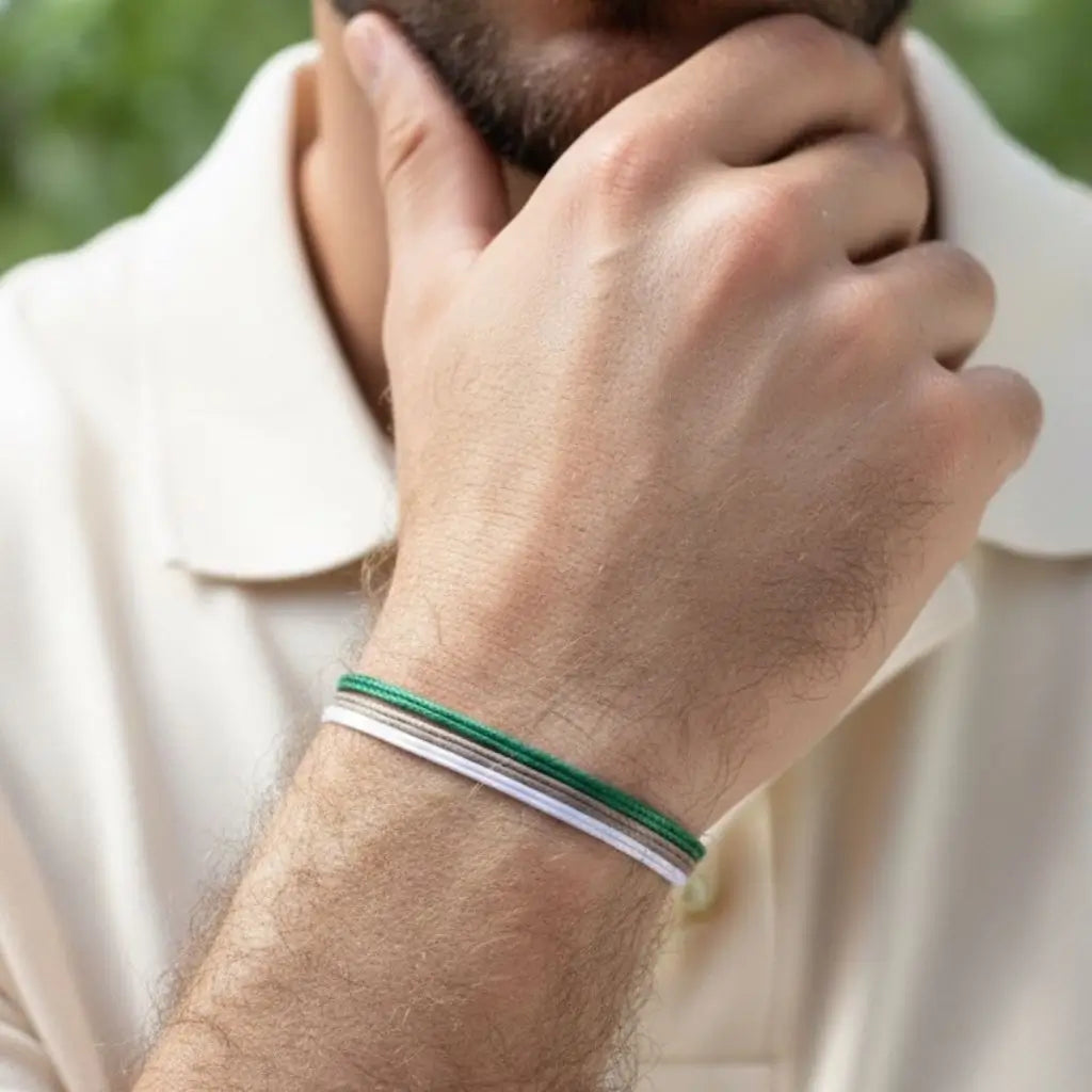 Close-up of a person wearing a green taupe and white bracelet on a blurred natural background