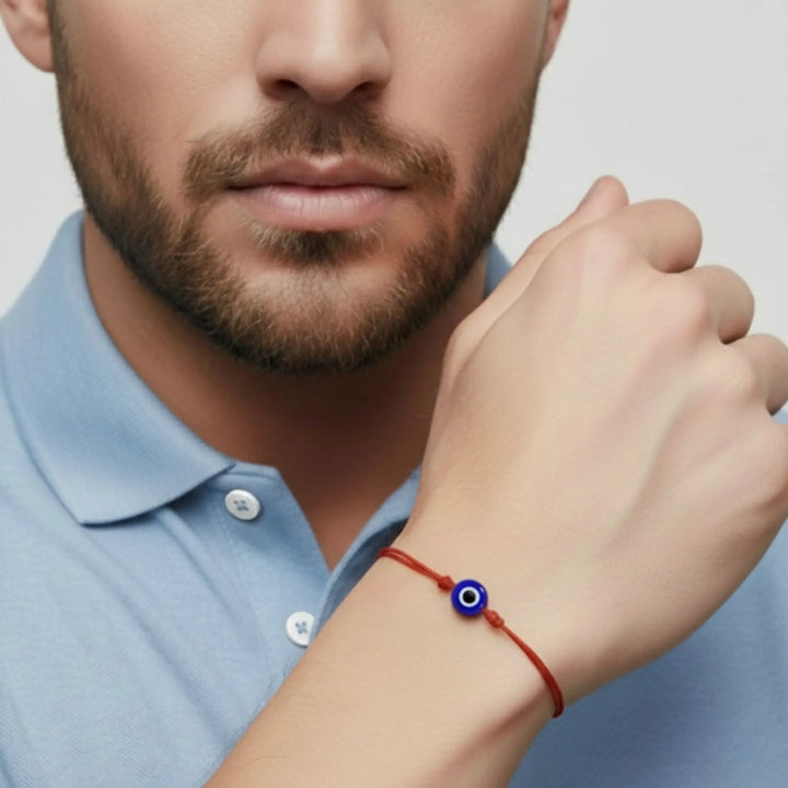 Man wearing a red bracelet with a blue evil eye charm on a plain background