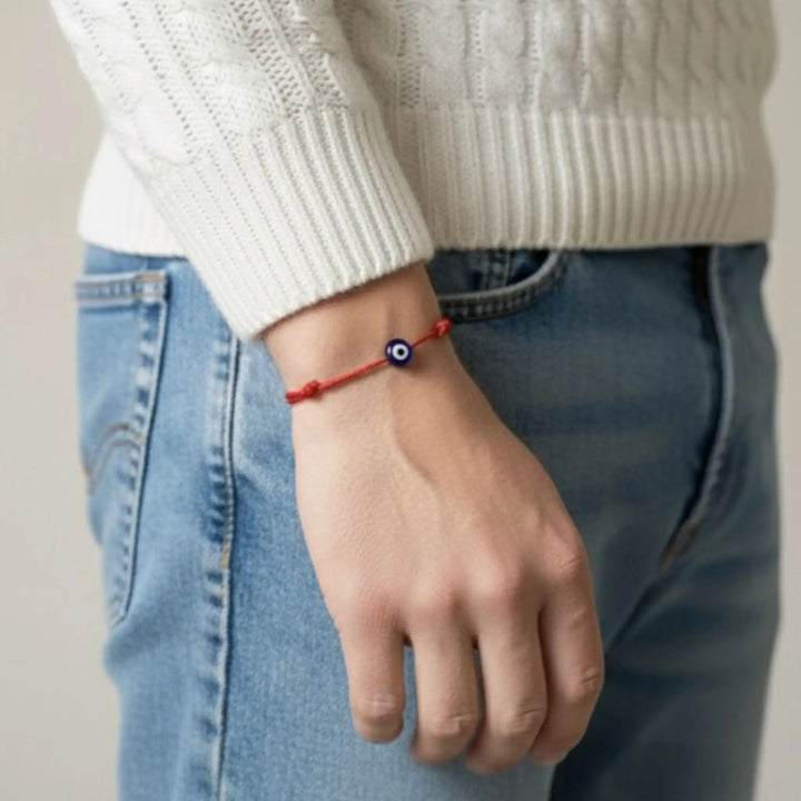 Person wearing a red bracelet with a blue bead on a neutral background