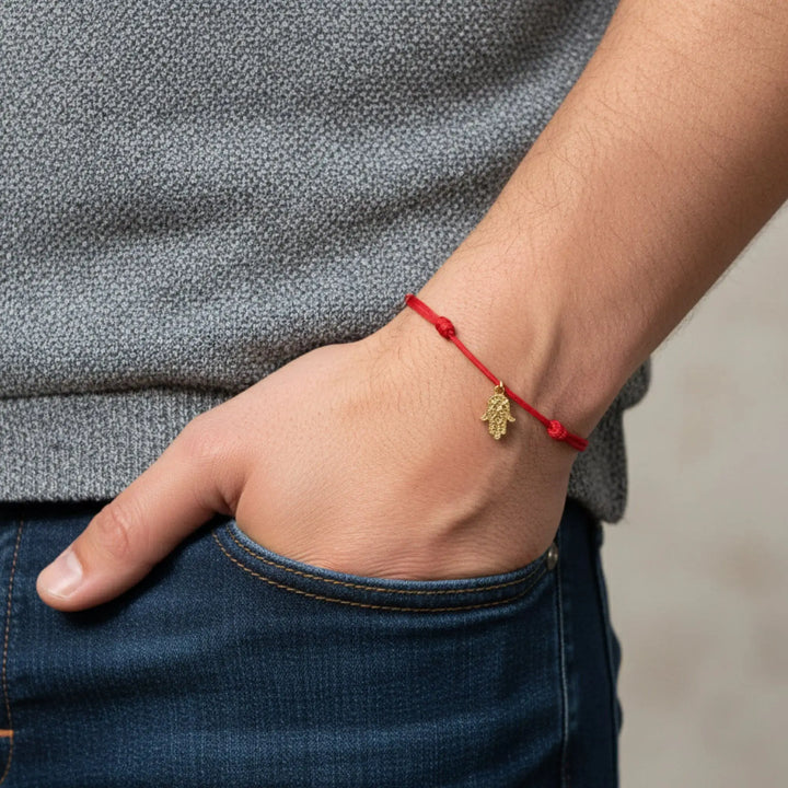 Person wearing a red string bracelet with a gold hamsa charm on a neutral background