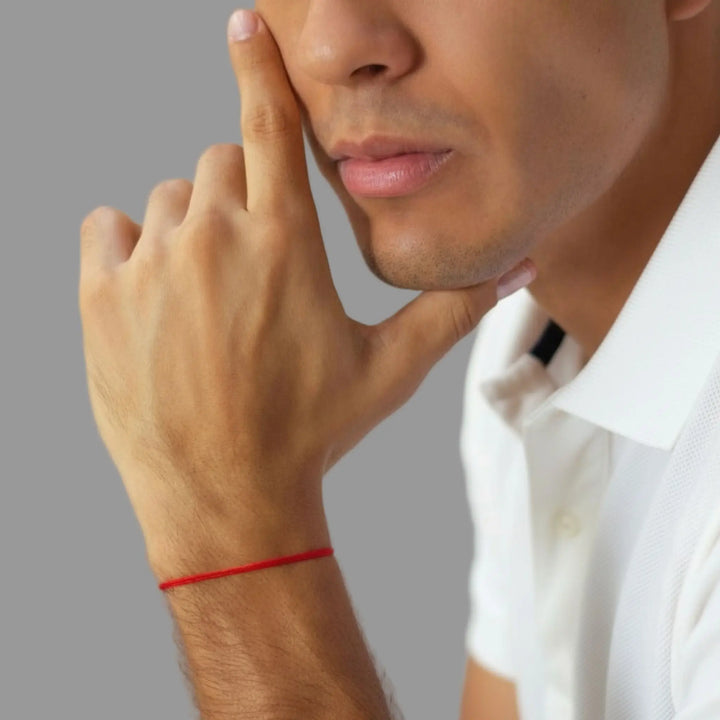 Man with a red string bracelet on his wrist, wearing a white shirt.