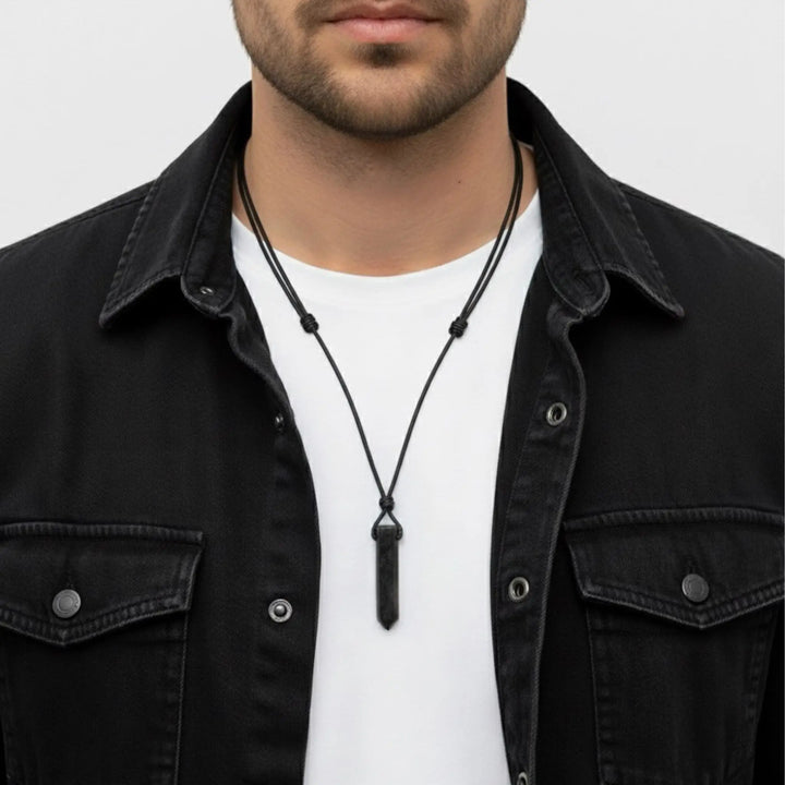 Man wearing a black tourmaline  necklace with a white shirt and black jacket on a light gray background
