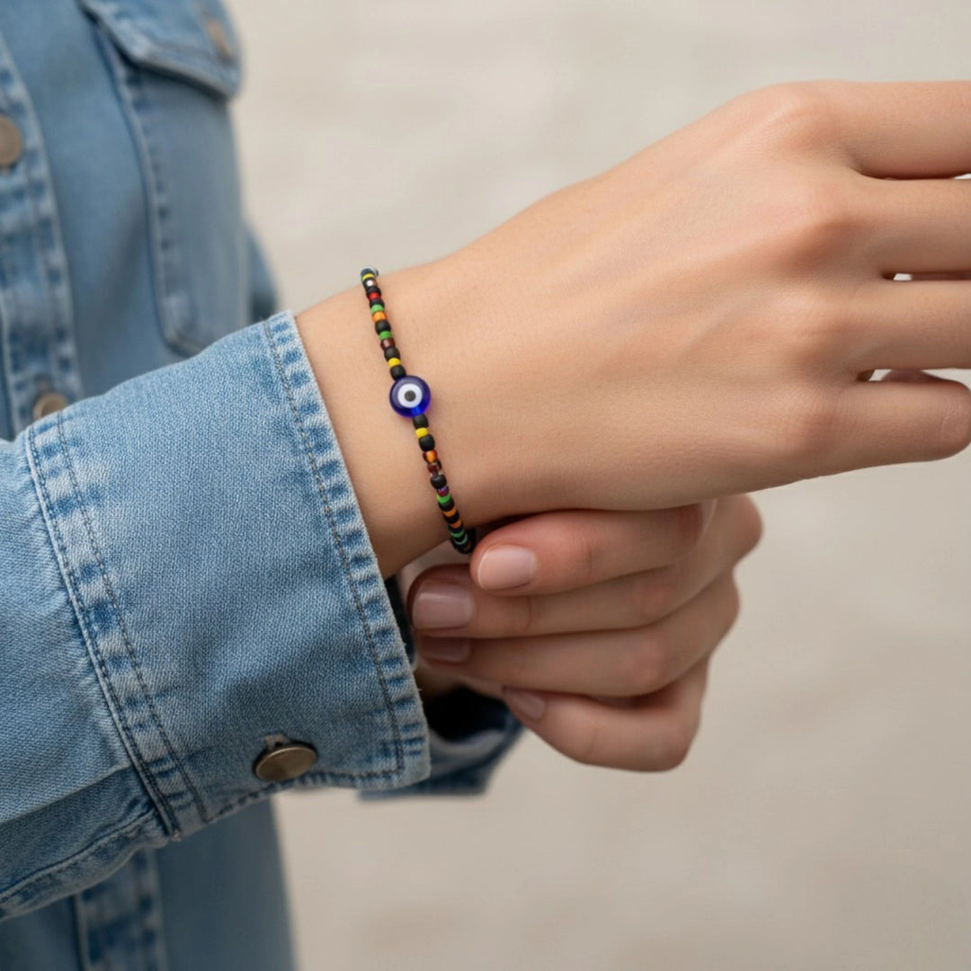 Hand wearing a colorful beaded bracelet with an eye charm, against a neutral background.