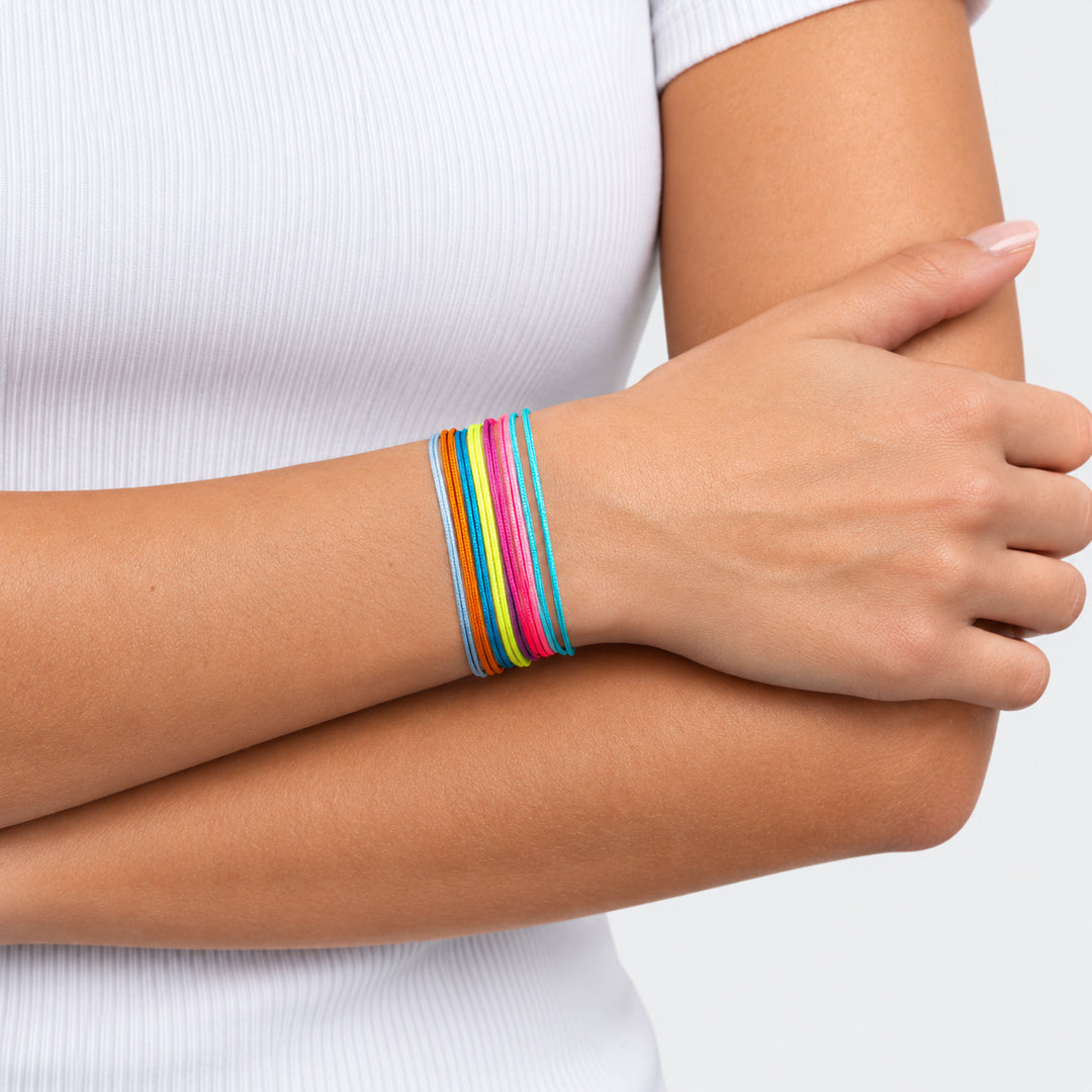 Woman wearing a stack of colorful nylon cord bracelets with her arms crossed over a white ribbed top.