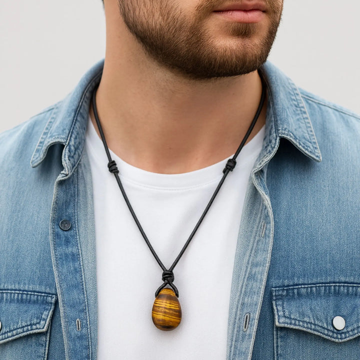 Man wearing a denim jacket with a necklace featuring a tiger eye pendant.