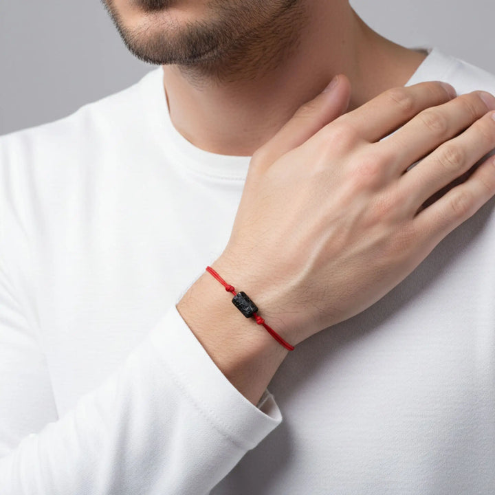 Person wearing a red and black tourmaline bracelet on a plain background