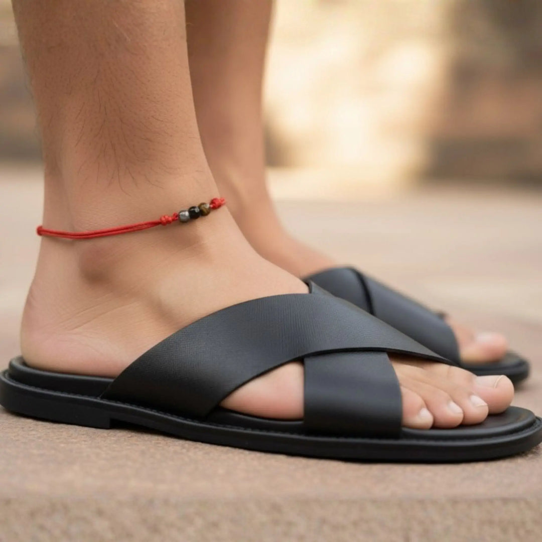 Black sandals worn with a red anklet a blurred background