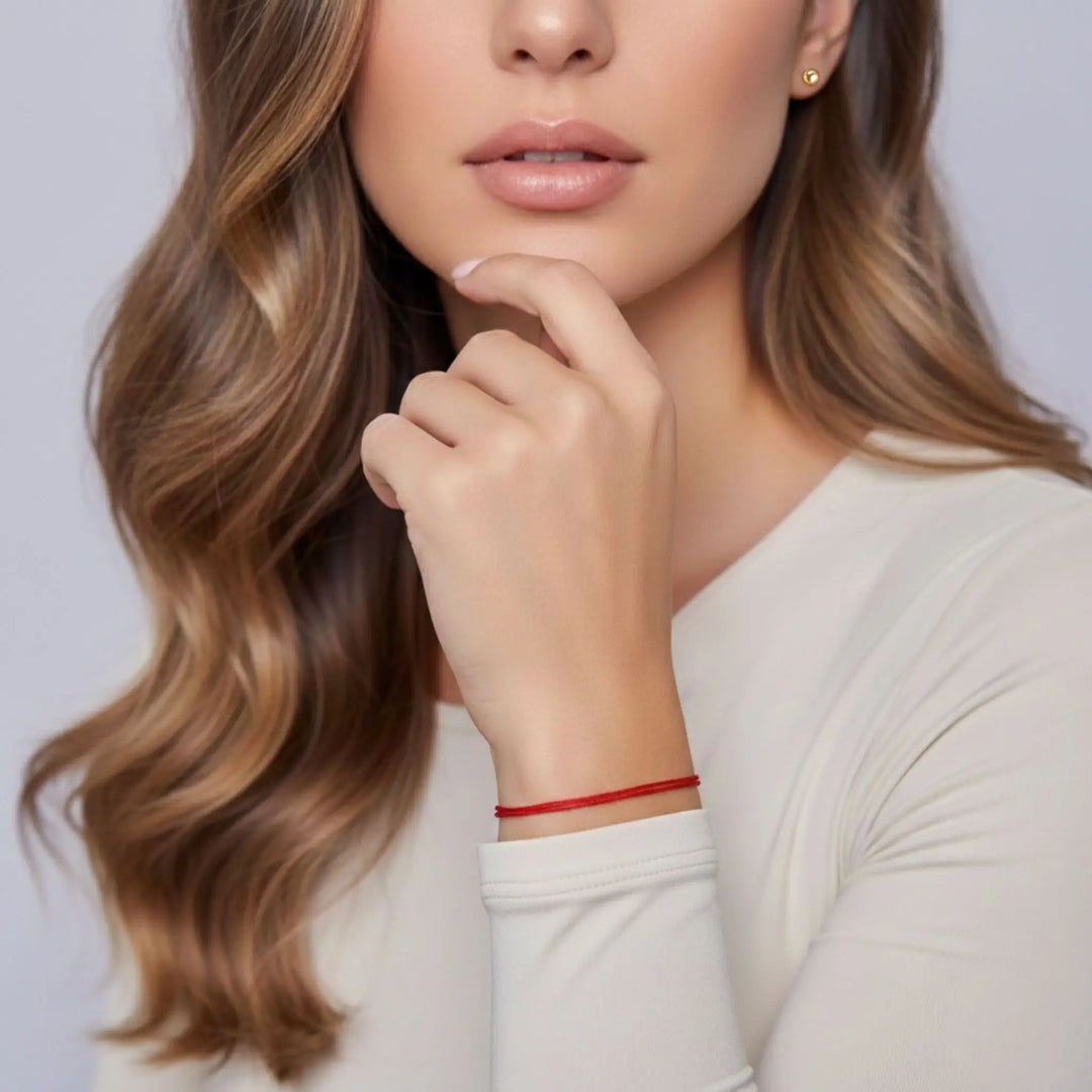 Woman with wavy hair wearing a red bracelet on a plain background