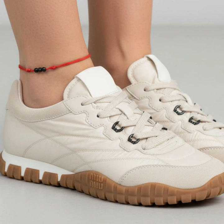 Black string anklet with three natural black tourmaline beads on a woman’s ankle, styled with beige sneakers with brown soles worn by a person on a light gray background