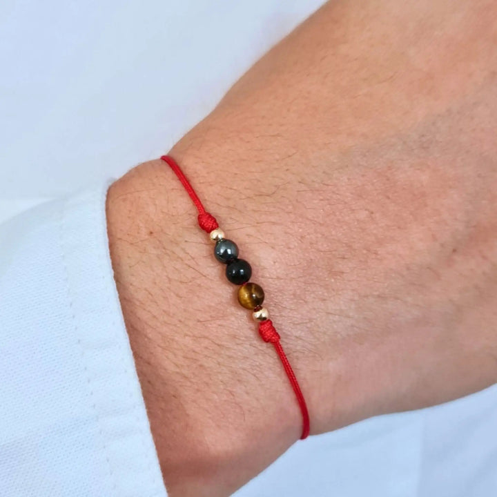 Ankle bracelet with red string and multicolored beads on a light blue background