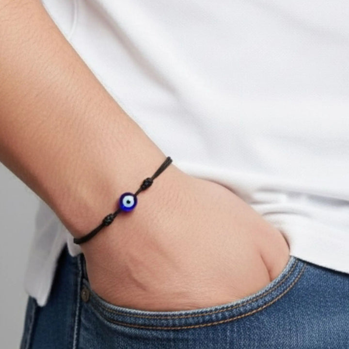 Black bracelet with a blue evil eye charm on a wrist against a white background