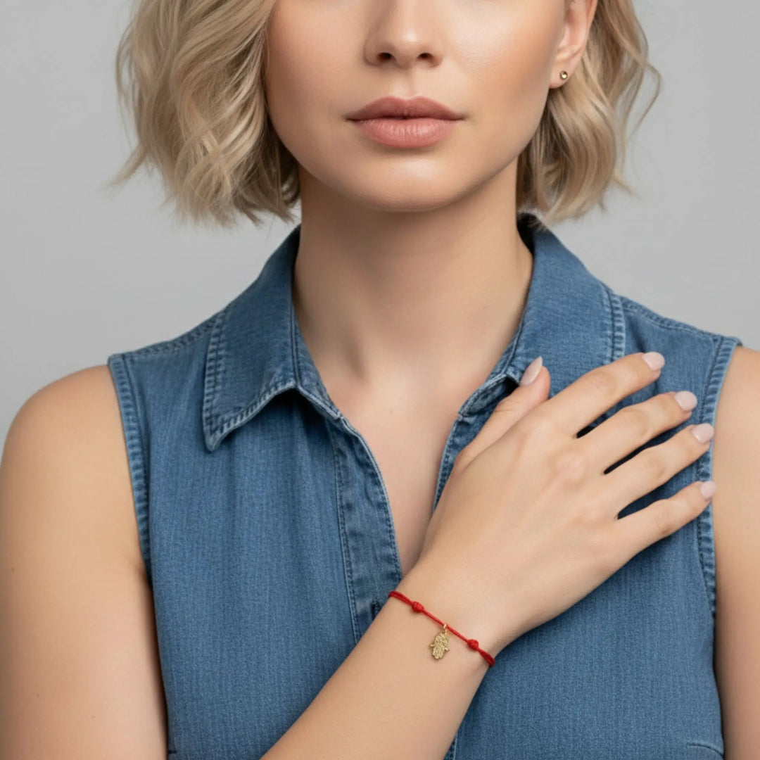 Woman wearing a red gold hamsa bracelet with a gold charm on a gray background