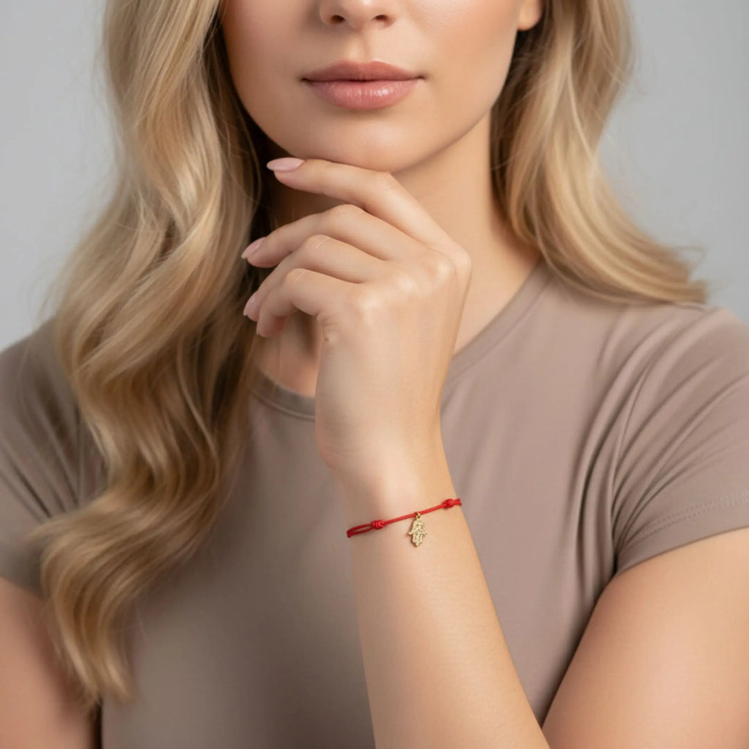 Woman wearing a red gold hamsa bracelet with a neutral background