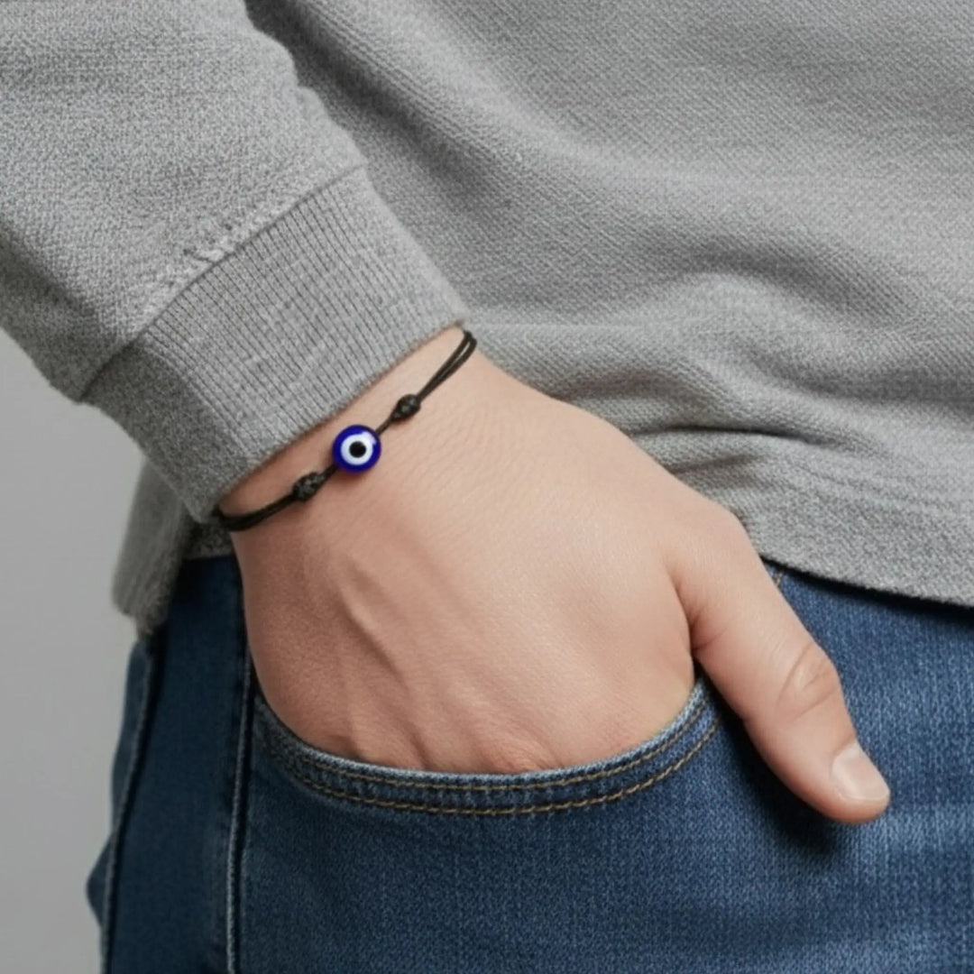 Hand wearing a bracelet with an eye charm, gray sweater and blue jeans.