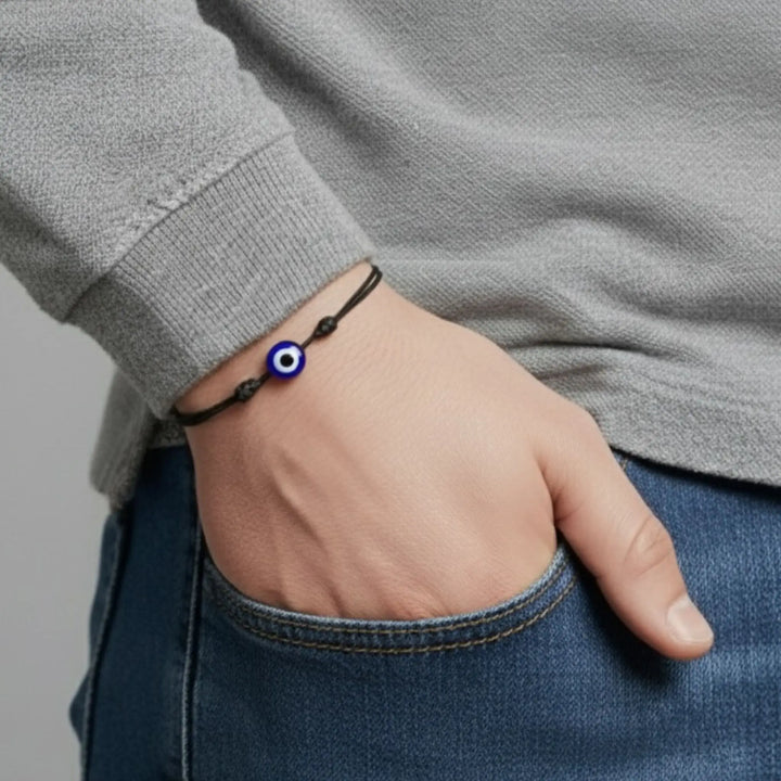 Hand wearing a bracelet with an eye charm, gray sweater and blue jeans.