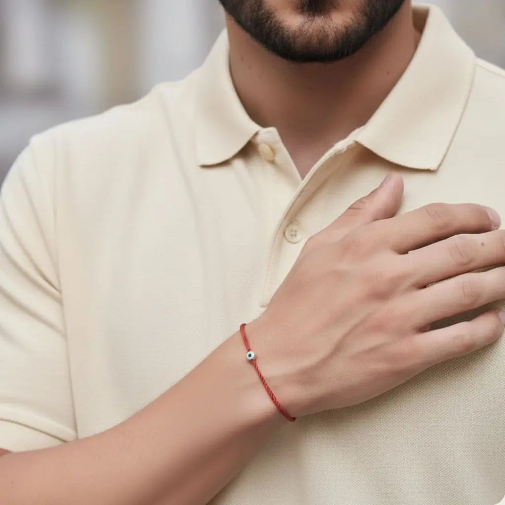 Person wearing a beige polo shirt with a red gold evil eye bracelet on a blurred background
