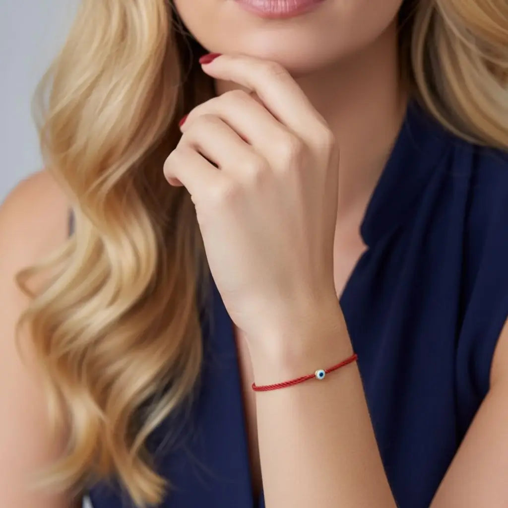 Woman wearing a red bracelet with a small gold evil eye charm, posing thoughtfully.