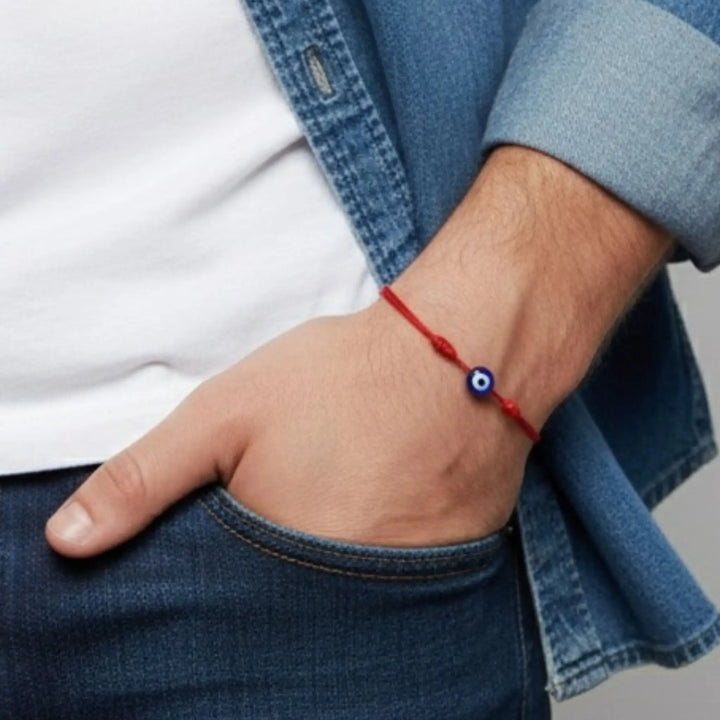 Person wearing a red bracelet with a blue evil eye bead on a neutral background