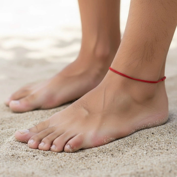 Mens feet on sand with a red anklet