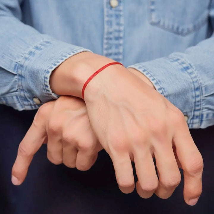 Close-up of a person's wrist with a red bracelet against a blue denim shirt 