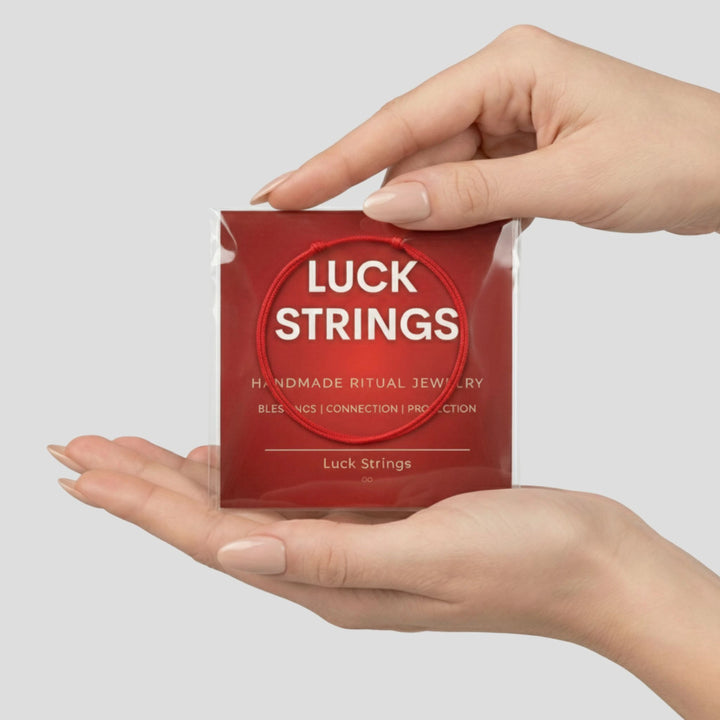 Red packaging of Luck Strings jewelry held by a hand on a light gray background