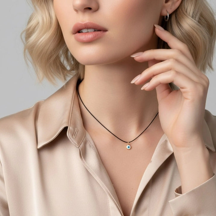 Woman wearing a necklace with a small round evil eye pendant, touching her ear against a neutral background