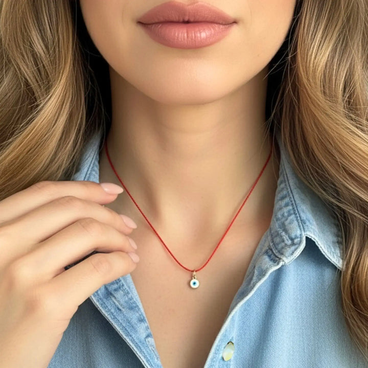 Close-up of a person wearing a red evil eye necklace with a small pendant, set against a neutral background.