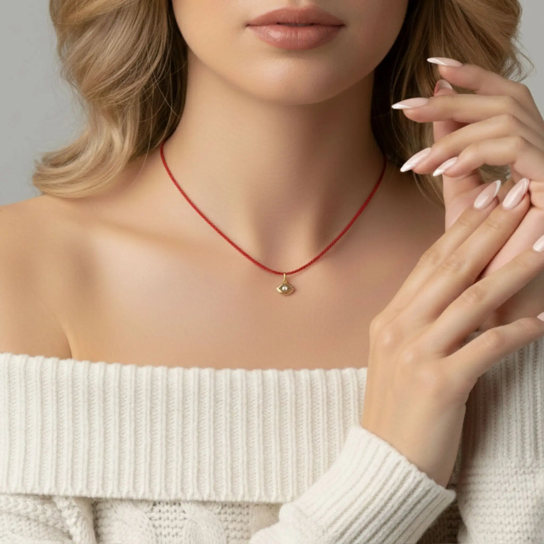 Woman wearing a red silk necklace with a small pendant, holding her hands near her face.
