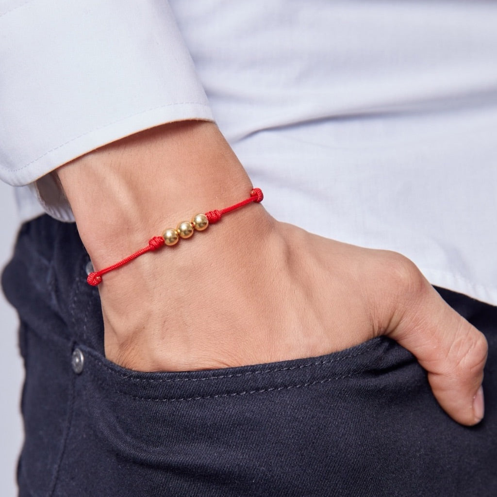 A person's wrist wearing a red knotted bracelet with gold beads.