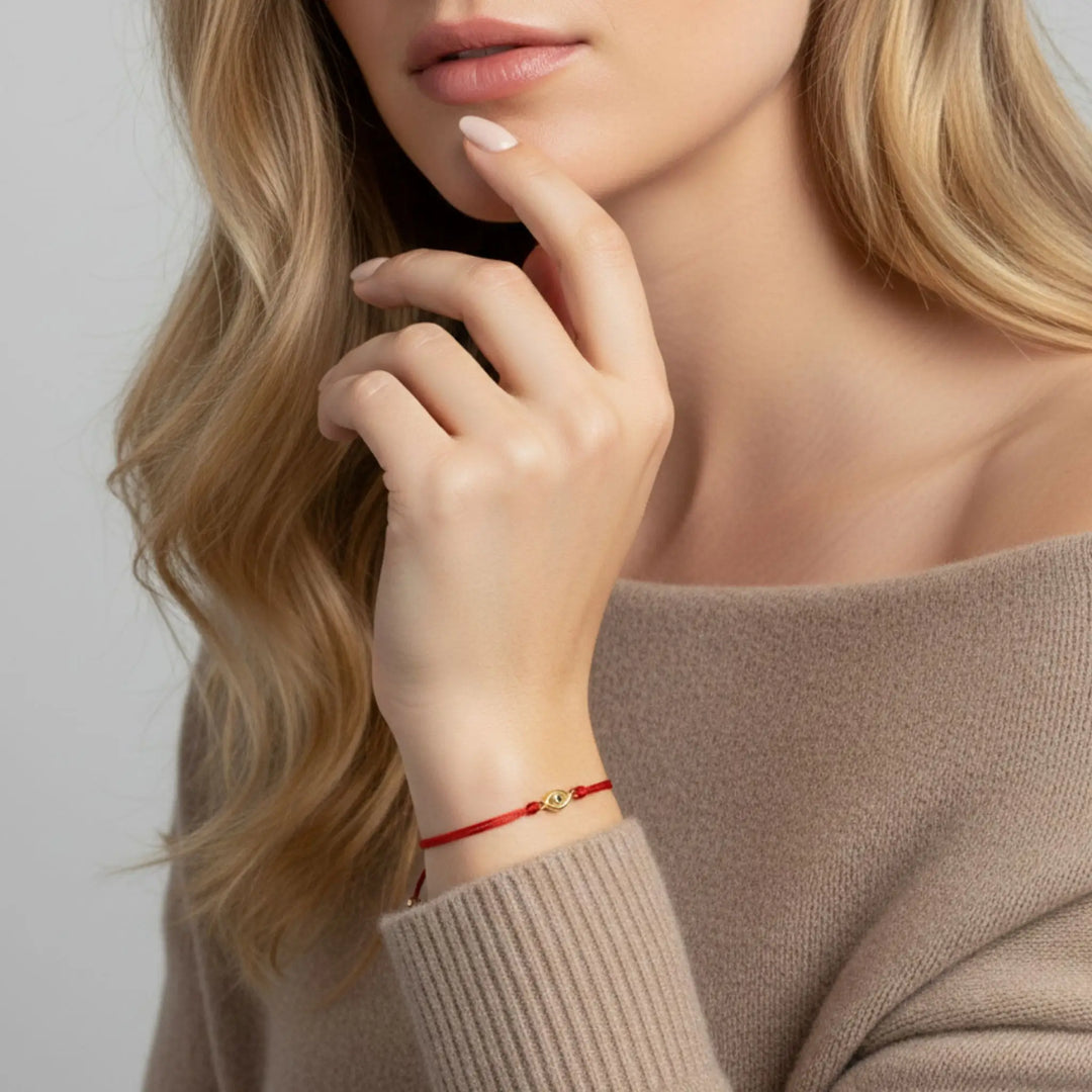 Woman wearing a red gold evil eye  bracelet on a plain background