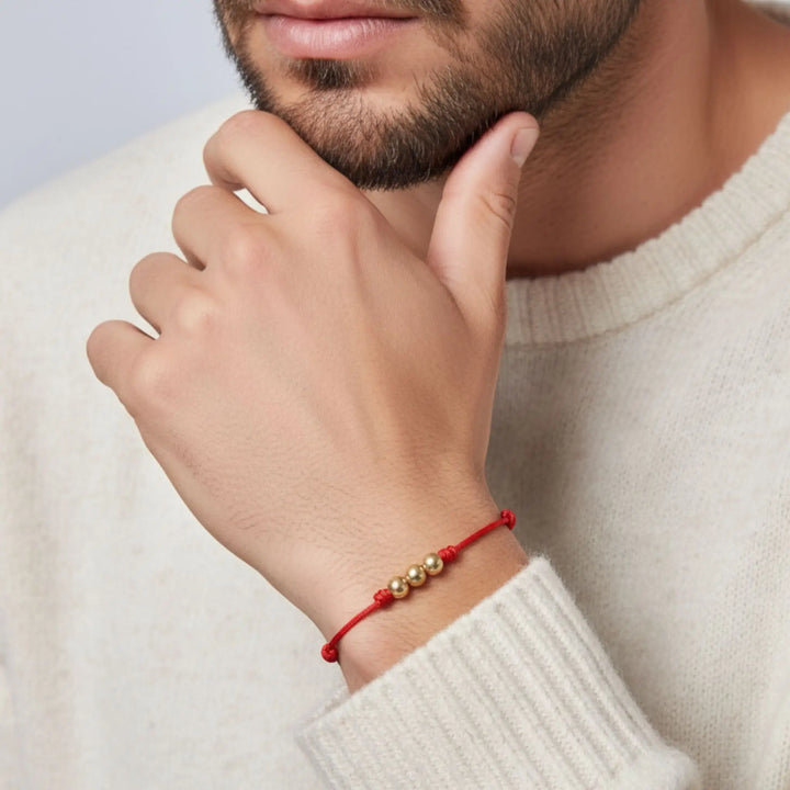Close-up of a person wearing a red bracelet with gold beads on a light background