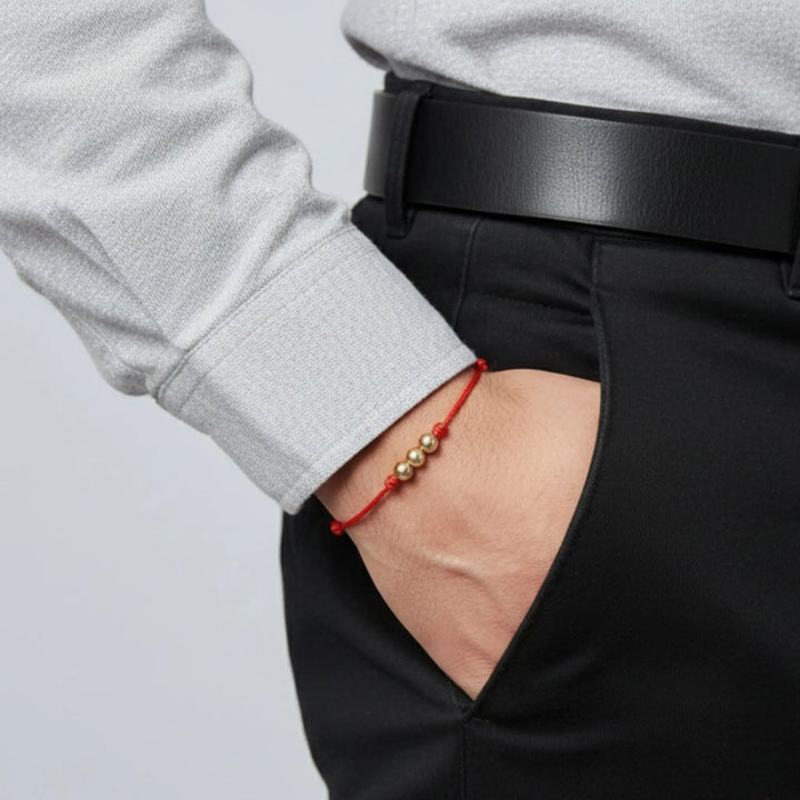 Person wearing a red bracelet with gold beads, partially tucked into black pants.