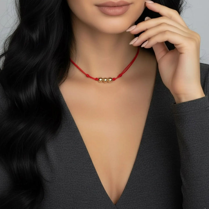 Woman wearing a red necklace with gold beads against a neutral background