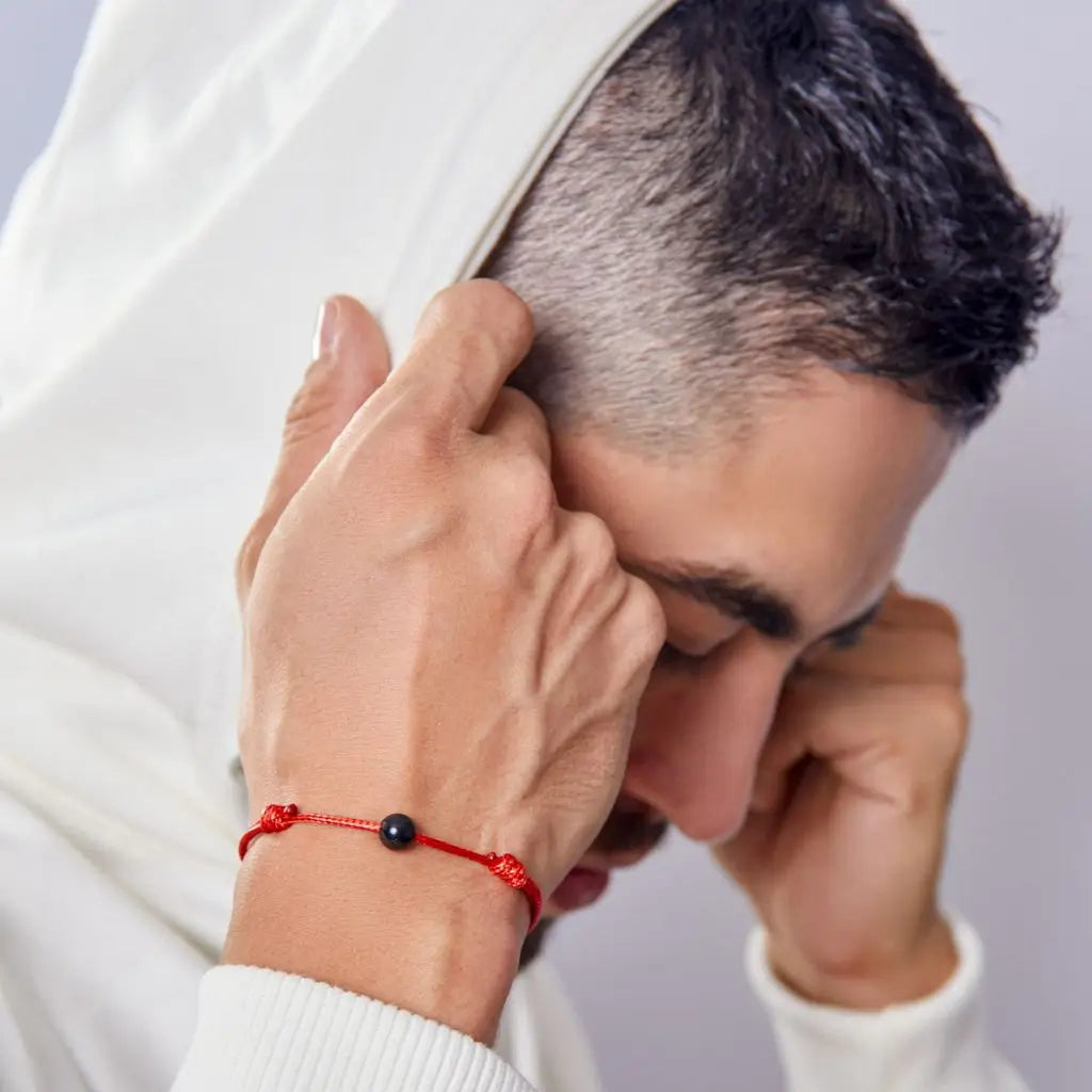 Men wearing a red bracelet with a black tourmaline bead on a plain background