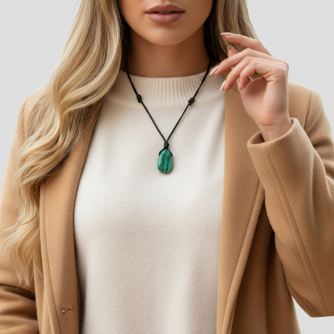 Woman wearing a beige coat and white sweater with a green malachite pendant necklace.