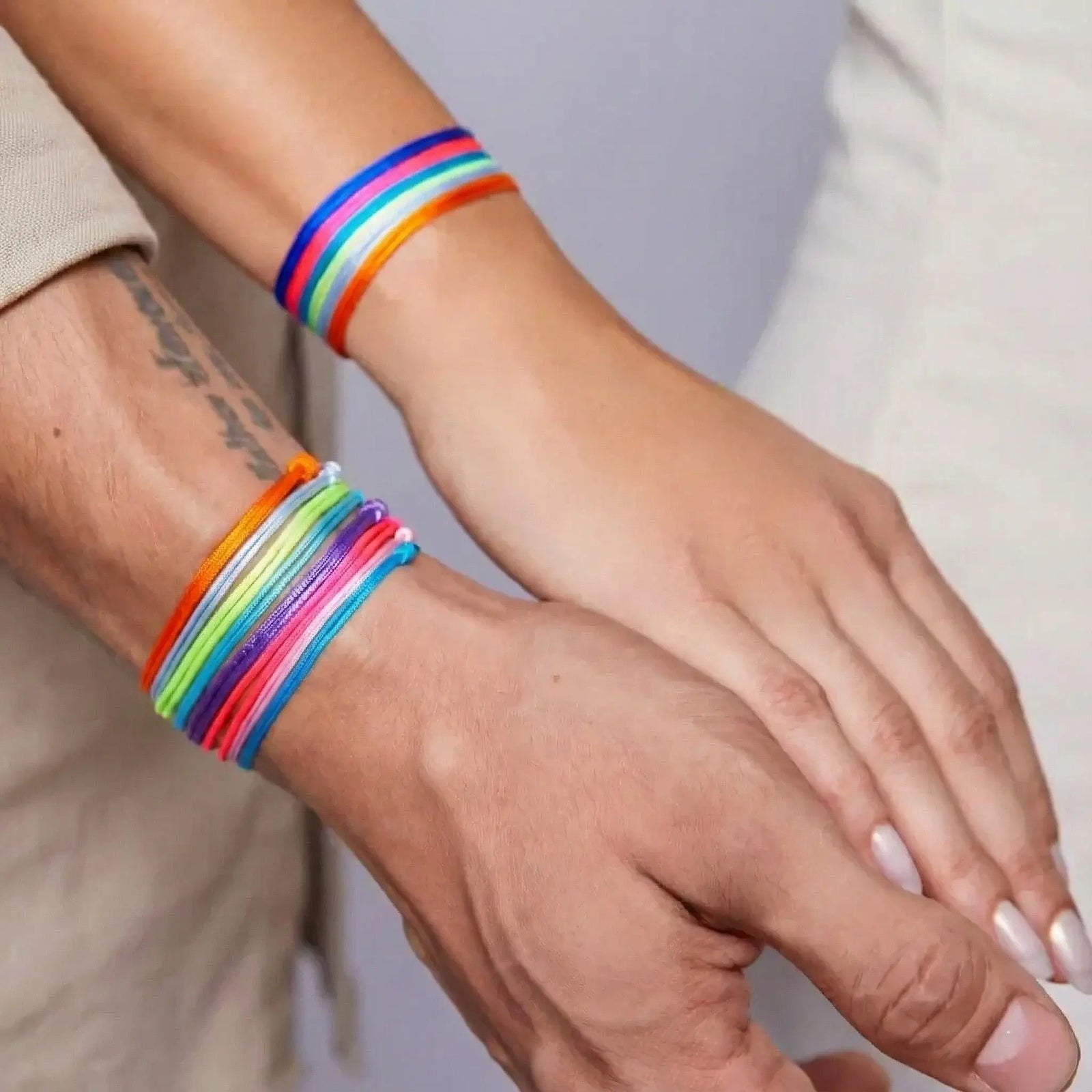Close-up of hands wearing colorful string bracelets on a neutral background
