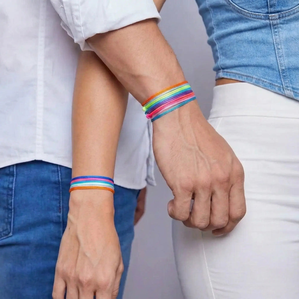 Two people holding hands with colorful bracelets on a neutral background