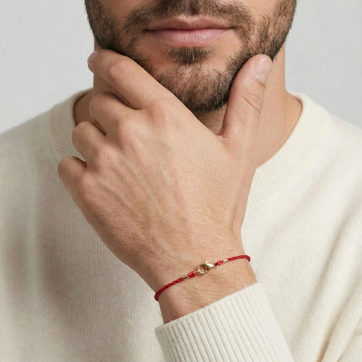Man wearing a solid gold clasp red bracelet with a gold charm on a plain background